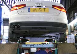 a white audi a4 high in the air on a ramp viewed from underneath receiving parts after failing its annual mot test