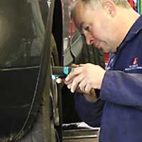 close up of an mot tester inspecting under a volkswagen rear drivers side wheel arch aided by a hand light for possible MOT failures