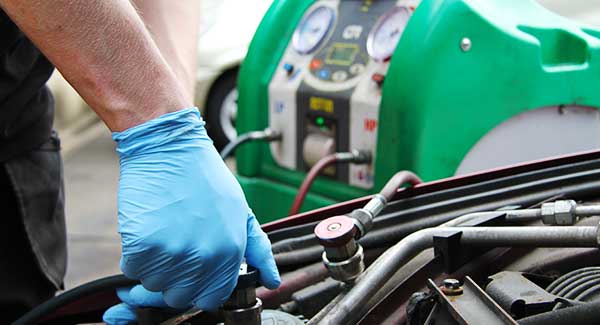 close up of an air conditioning experts blue gloved hands connecting a car to air con regas equipment