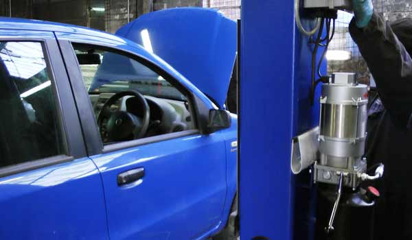 side view behind a lilac blue ramp post with a service mechanic pressing the ramp up button and a blue volkswagen on the ramp with bonnet up awaiting a servcie