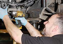 distance side view of our clutch specialist replacing a clutch on a ford with the car in the air on a ramp and partially dismantled still using an impact air driver to remove the clutch bolts in our well lit sheffield workshop