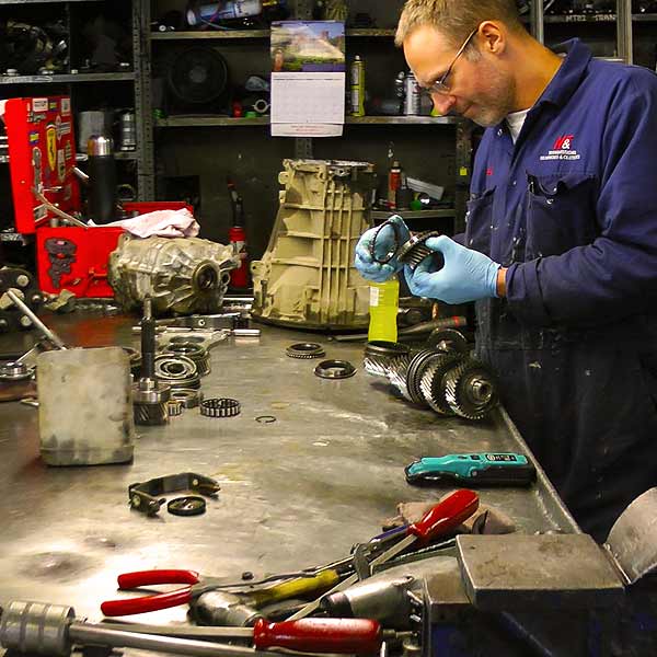 distance worshop view of a gearbox expert reconditioning a vw golf gearbox on a large metal bench with gear components and tools visible