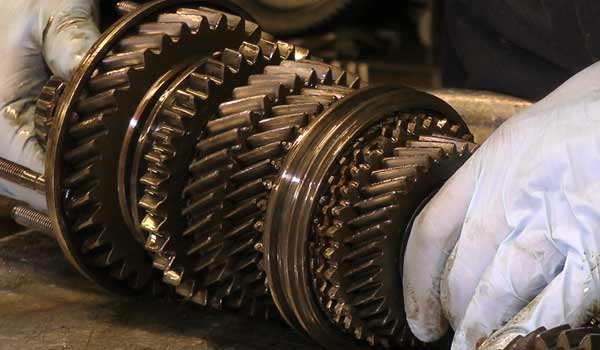 front close up view of a gearbox experts hands wearing light blue shiny gloves inspecting a vw golf gearbox layshaft for signs of damage and for reconditioning suitability