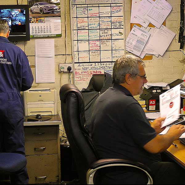 to the right a distance view of adrian working hard in admin doing a customers receipt and to the left an mot tester updating the mot test computer with details of a car on test which passed