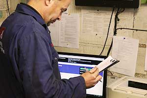 our mot specialist in blue overalls with m and t logo in the office looking at a sheet and updating the mot computer with details of a ford that has just passed its mot test