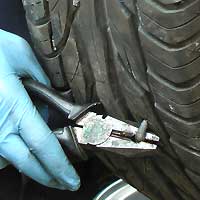 close up of a tyre punctured with a large screw which is being pulled out with heavy duty pliers before being repaired