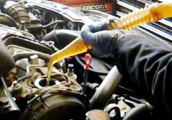 close up of a ford car engine receiving new oil from a clear spout poured by an expert mechanic sporting blue latex gloves as part of its service