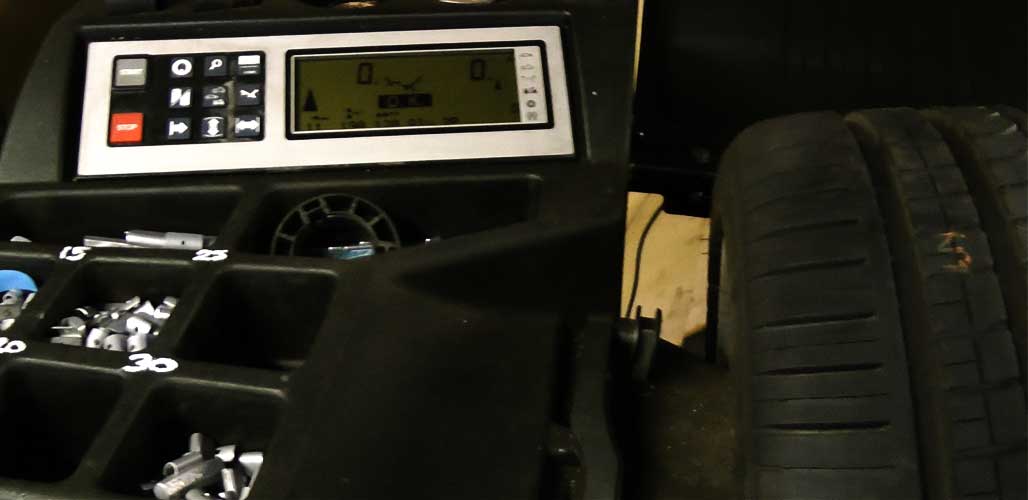 close up of garage wheel balancing equipment showing the digital display and its assorted coloured operational buttons as well as a vehicle wheel and tyre clamped to it
